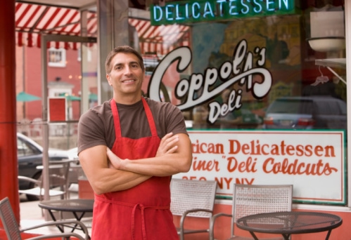 Mixed race business owner in apron in front of deli